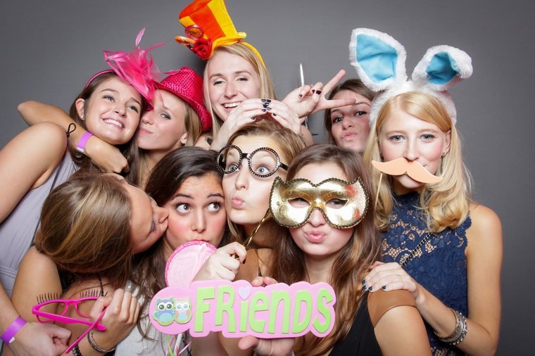 A group of friends posing with photo booth props against a studio backdrop