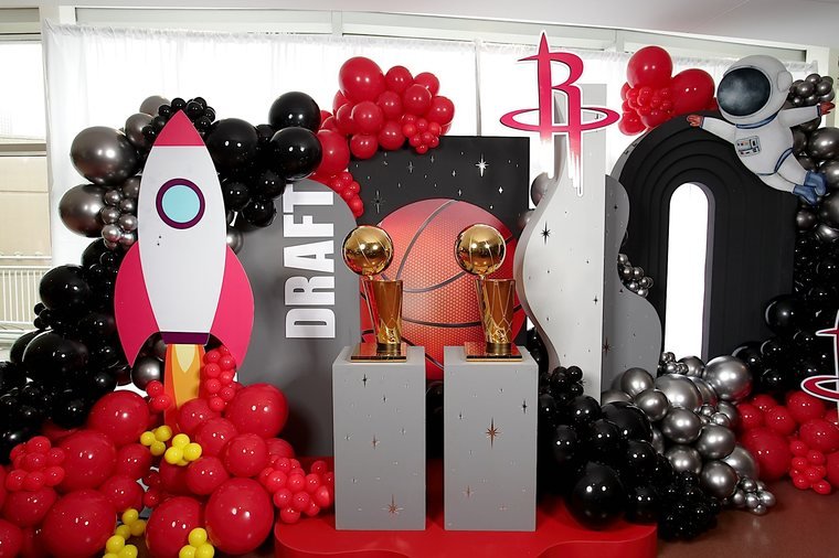 A Houston Rockets Draft Night photo backdrop with a rocket ship, astronaut, and championship trophies on display